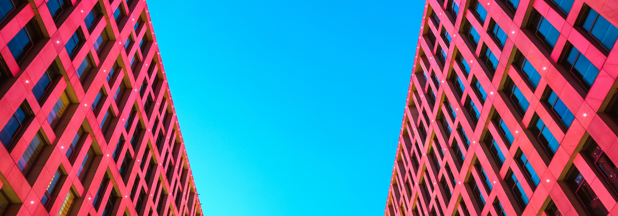 Two modern red skyscraper buildings with a strip of blue sky in between.