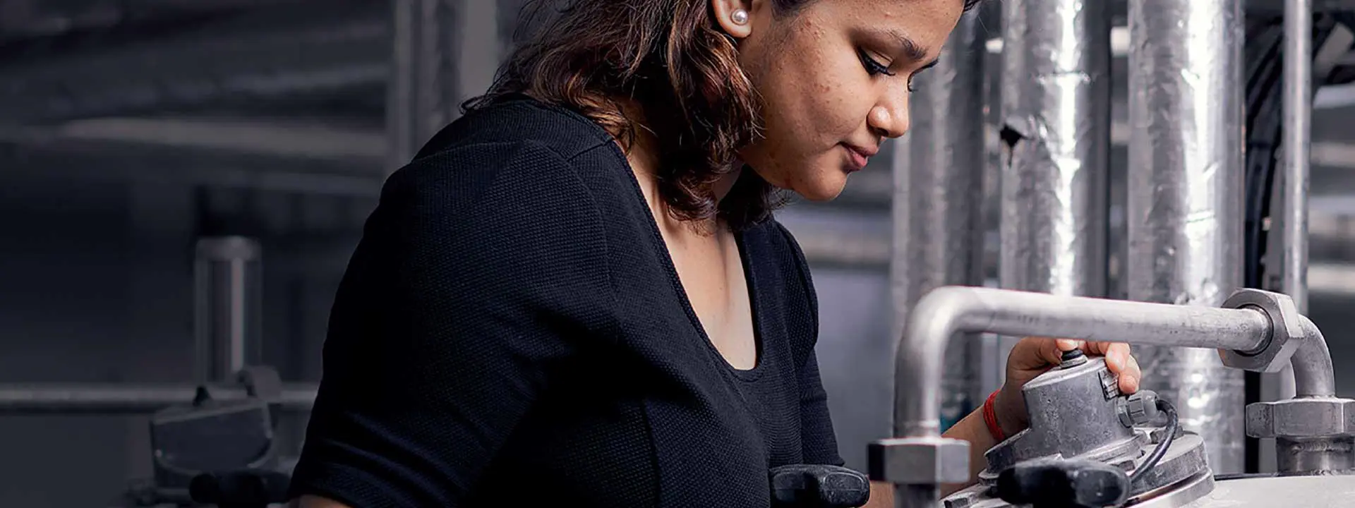 A woman wearing a black shirt is engaged in observing a pressure guage, demonstrating her skills and concentration..