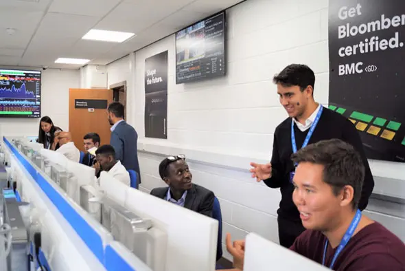 Individuals in a class sitting at computers and some in conversation.