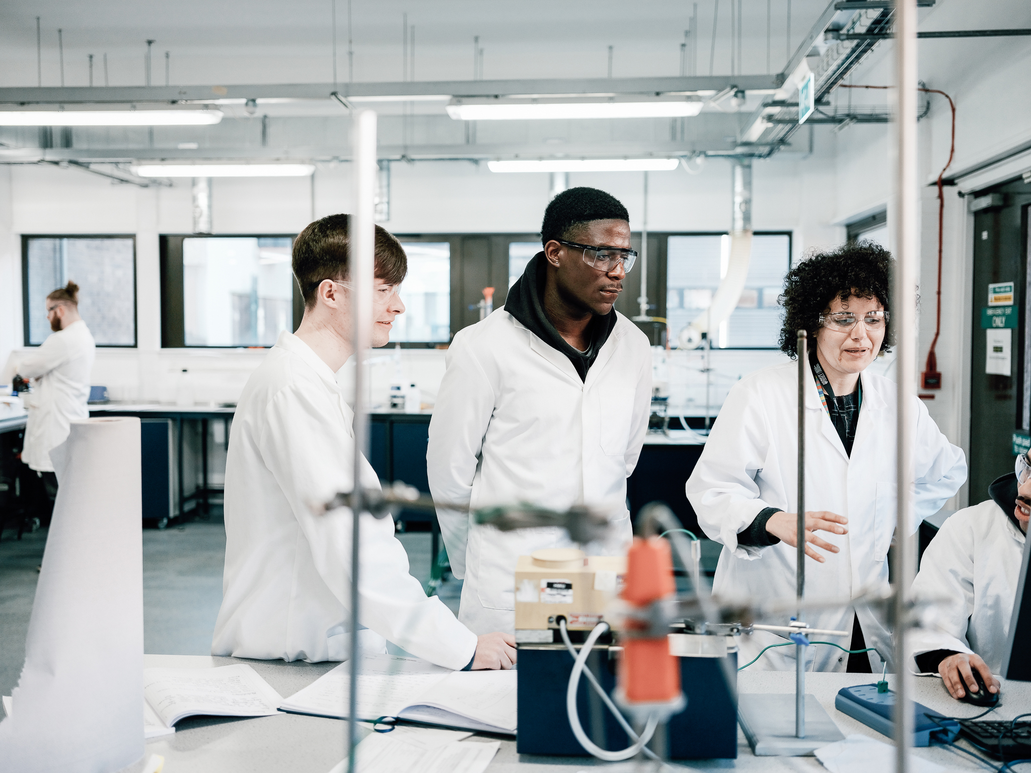 Two students observing a lab technician in a science and engineering lab.  