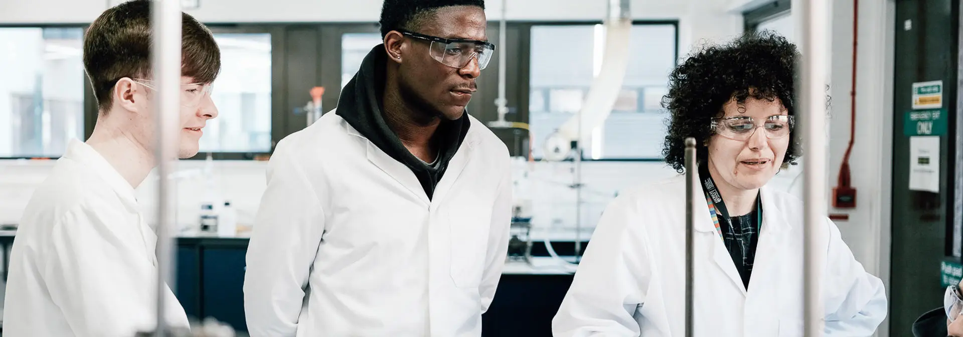 Two students observing a lab technician in a science and engineering lab.