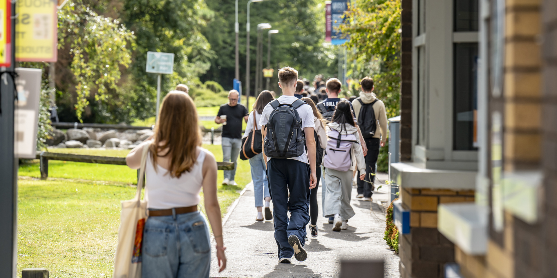 A group of students walking on a path, surrounded by grass and trees.