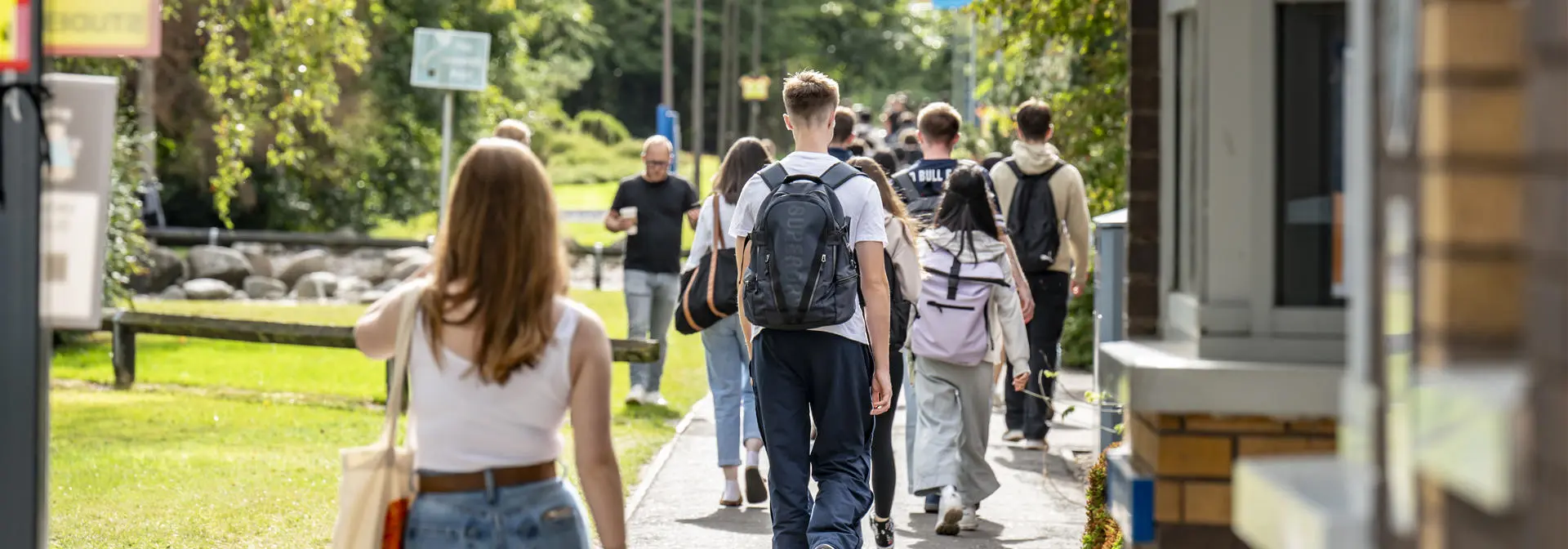 A group of students walking on a path, surrounded by grass and trees.