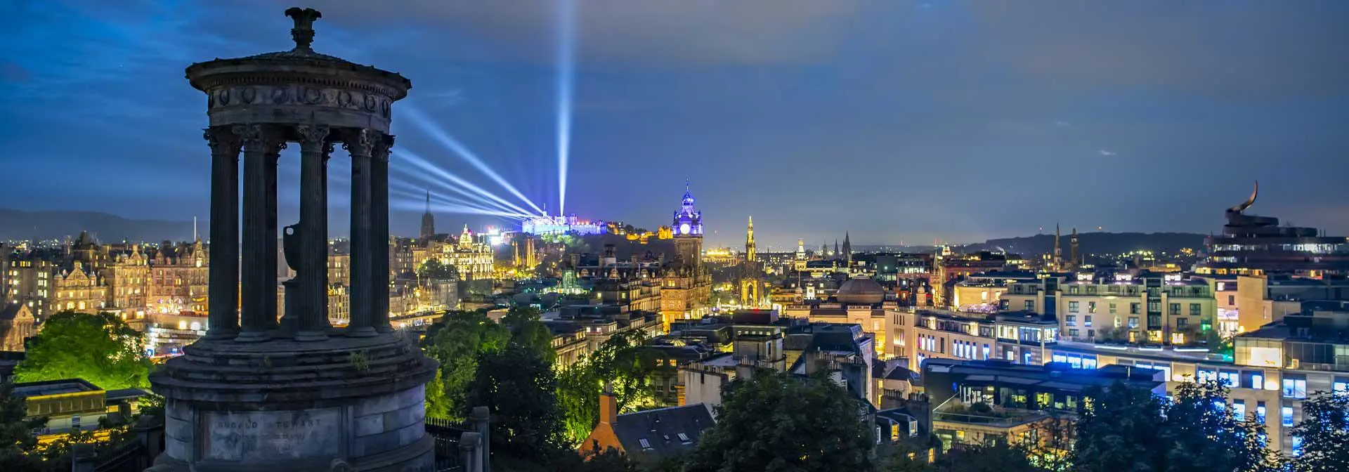 Edinburgh's Dugald Stewart monument and vibrant cityscape with twinkling lights and historic architecture.