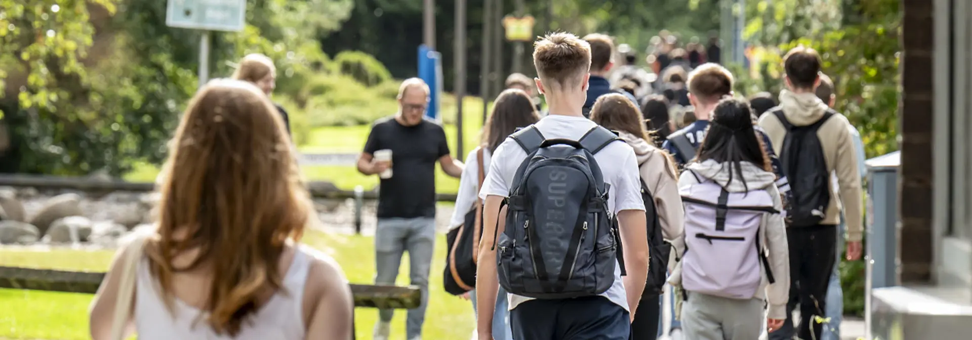 A group of students walking on a path, surrounded by grass and trees.