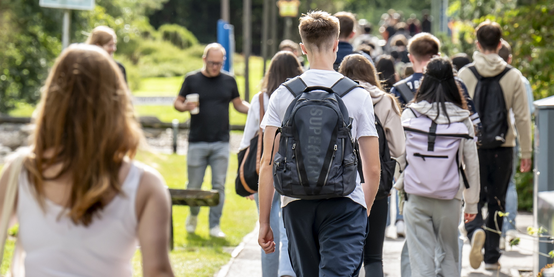 A group of students walking on a path, surrounded by grass and trees.