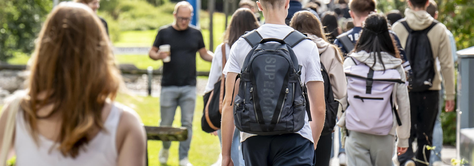 A group of students walking on a path, surrounded by grass and trees.
