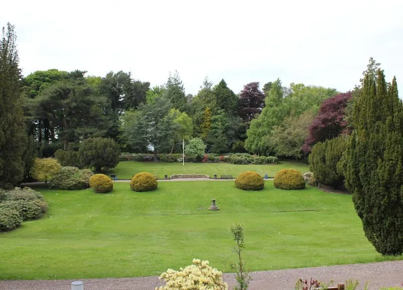 The Lawn viewed from the site of the old Riccarton House Garden lawn with large circular bushes, water fountain and tall trees