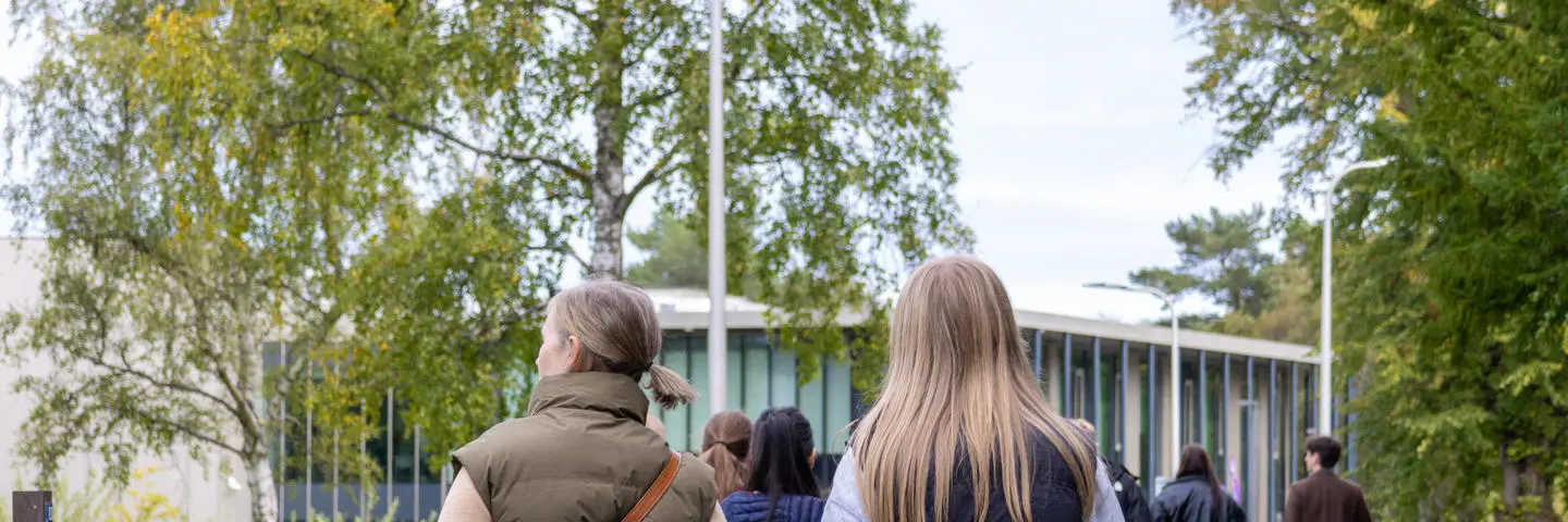 Individuals walking towards a building with trees and nature either side.