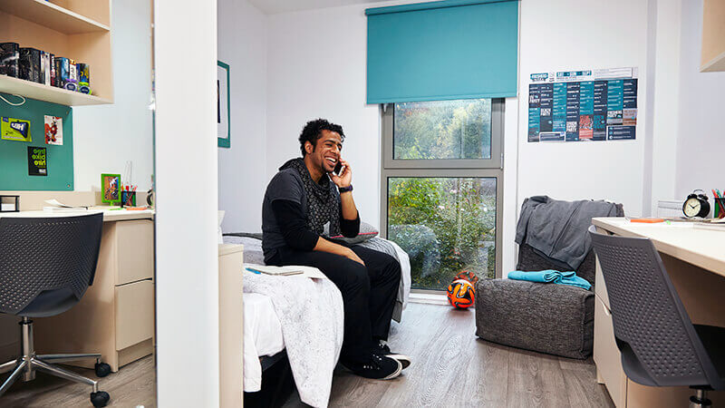 Student sitting on bed making phone call