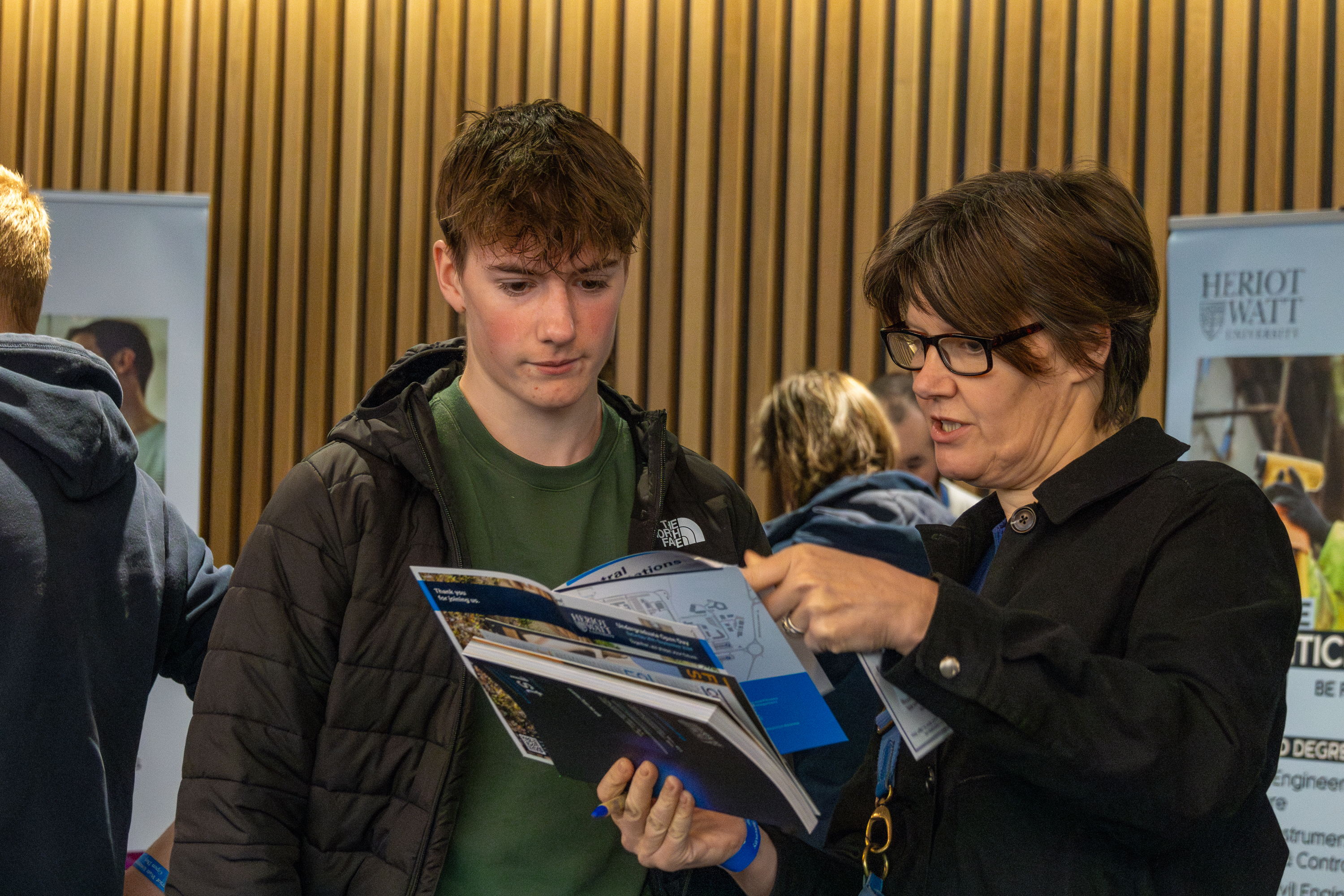 A woman discusses a Heriot-Watt prospectus with a young man