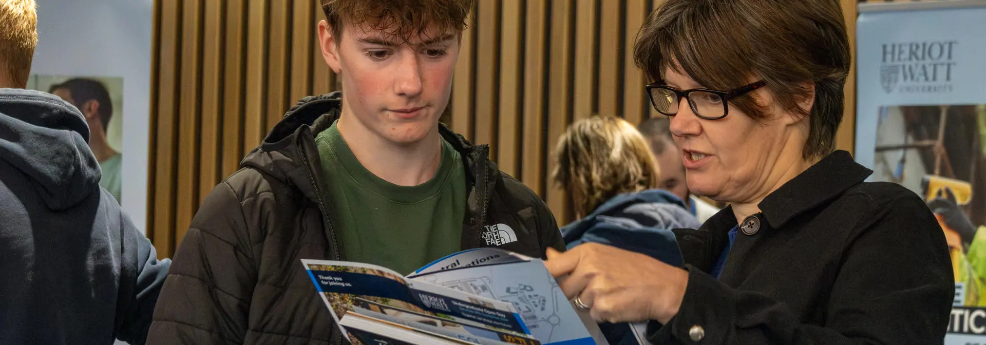 A woman discusses a Heriot-Watt prospectus with a young man