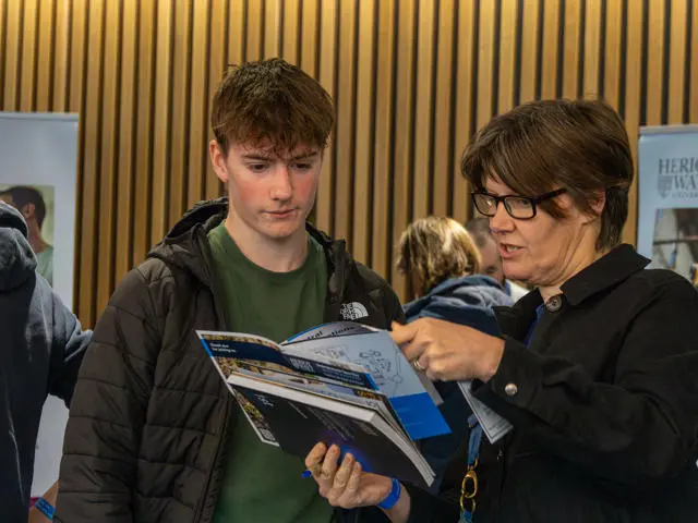 A woman discusses a Heriot-Watt prospectus with a young man