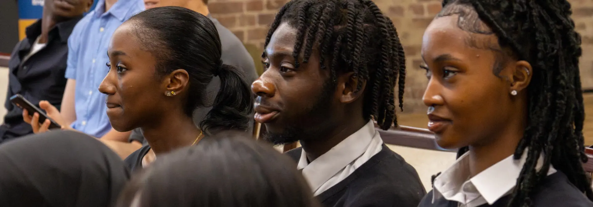 Three school students dressed in uniform staring focused at an event.