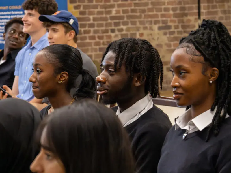 Three school students dressed in uniform staring focused at an event.