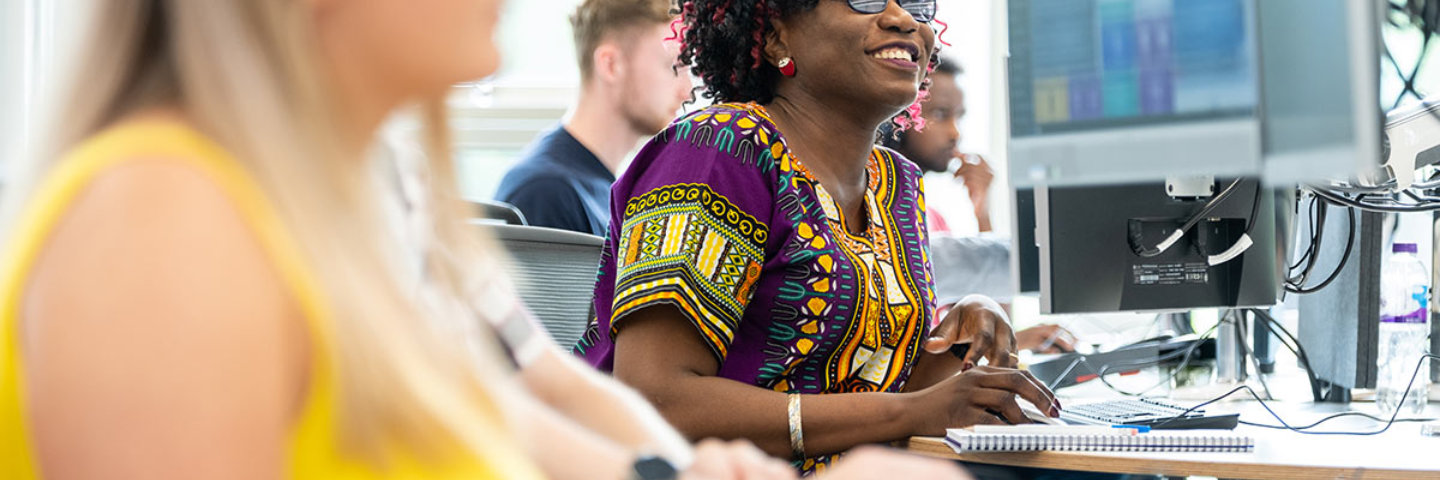 A smiling woman works at a desk and on a computer in an office.