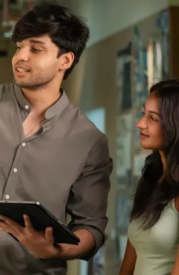 Two individuals standing and pointing to a wall of posters.
