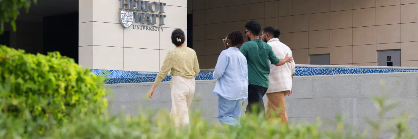 Four students walking towards the Heriot-Watt University Dubai campus entrance.