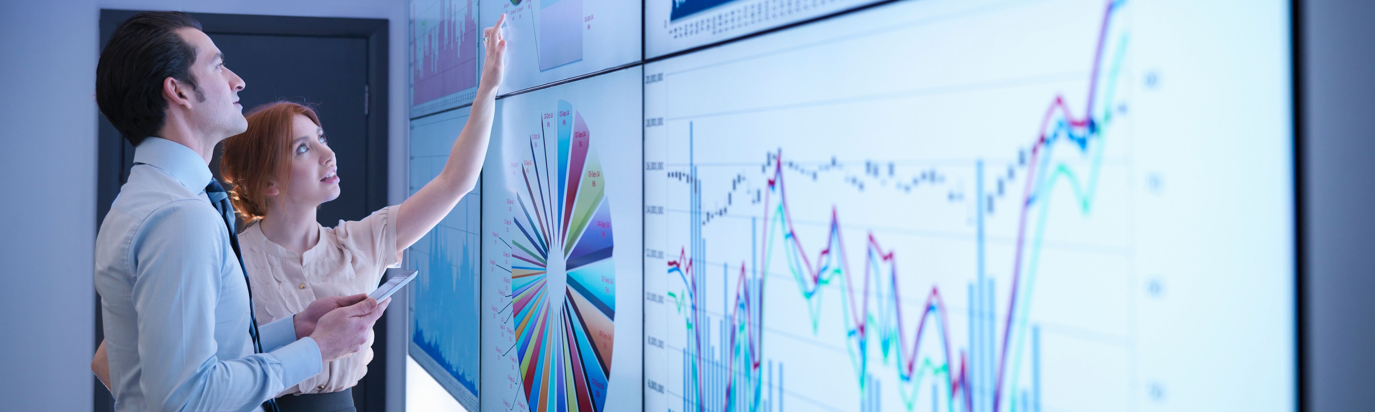 Two individuals discussing and reviewing graphs on a board.