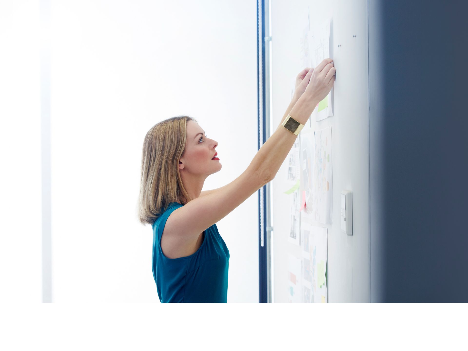 Woman pins paper to a board in a meeting room.