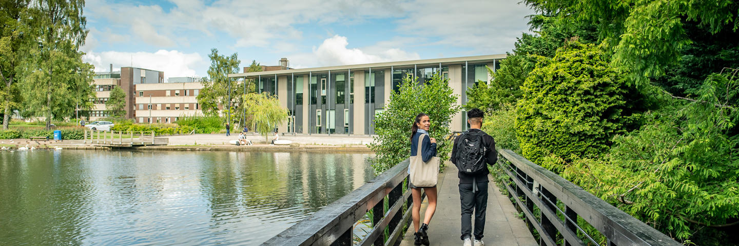 Two students walking across a bridge over a loch.