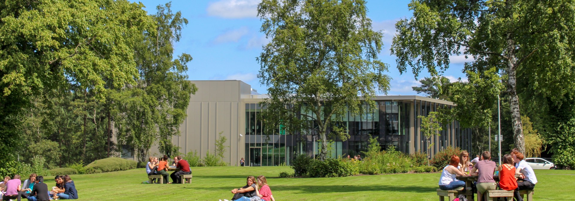 People sitting on benches and on a lawn of grass on the Heriot-Watt University Edinburgh campus
