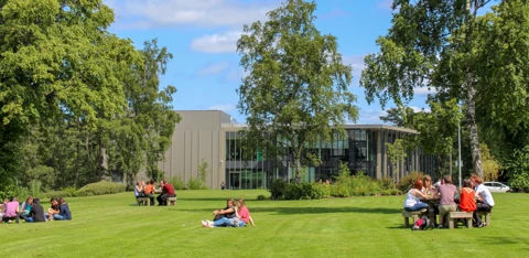 People sitting on benches and on a lawn of grass on the Heriot-Watt University Edinburgh campus