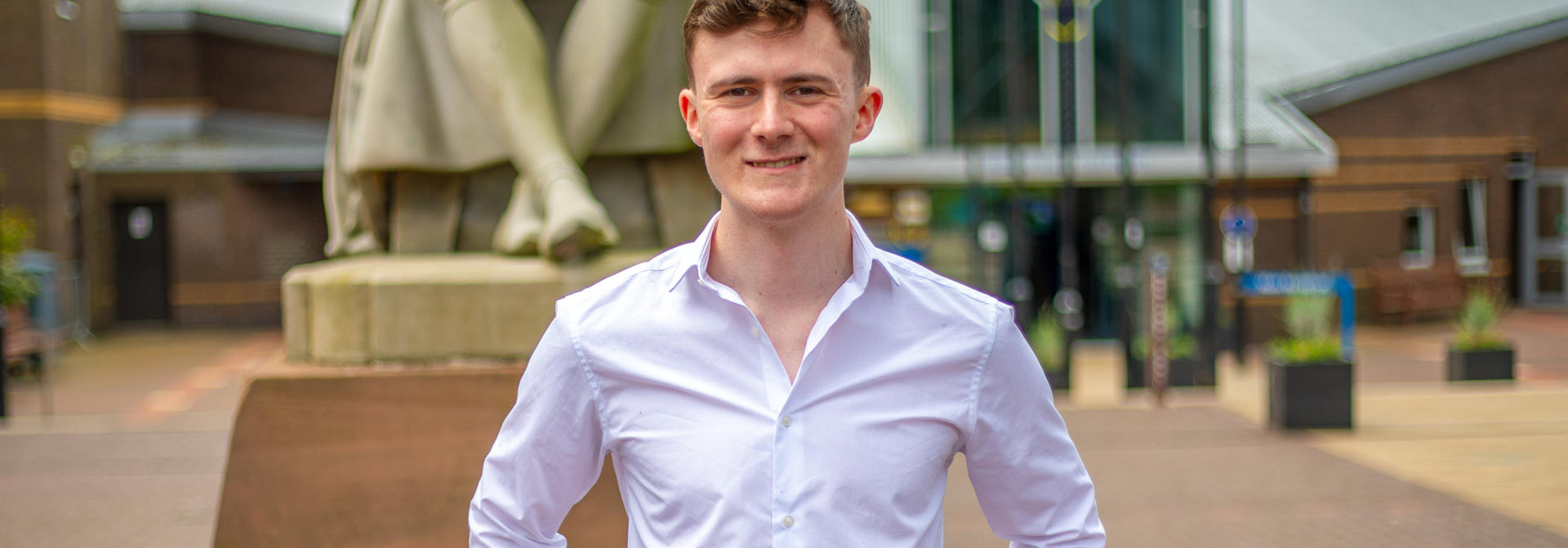 A man stands in front of a statue at the Heriot-Watt University Edinburgh campus.