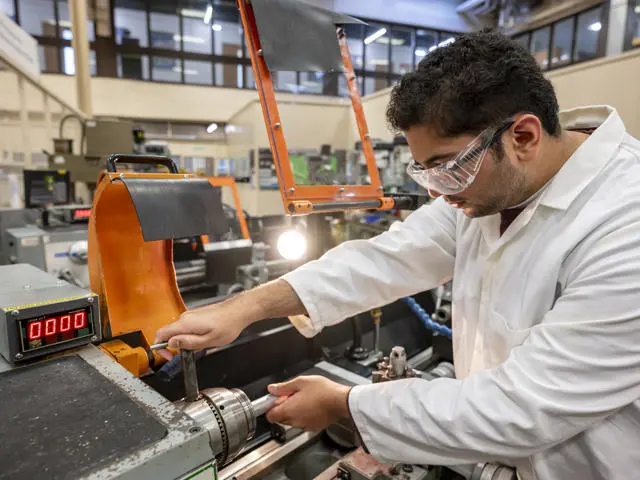 A student tightening a lathe in a large workshop