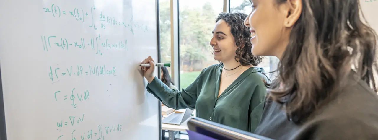 Two students writing maths equations on a whiteboard.
