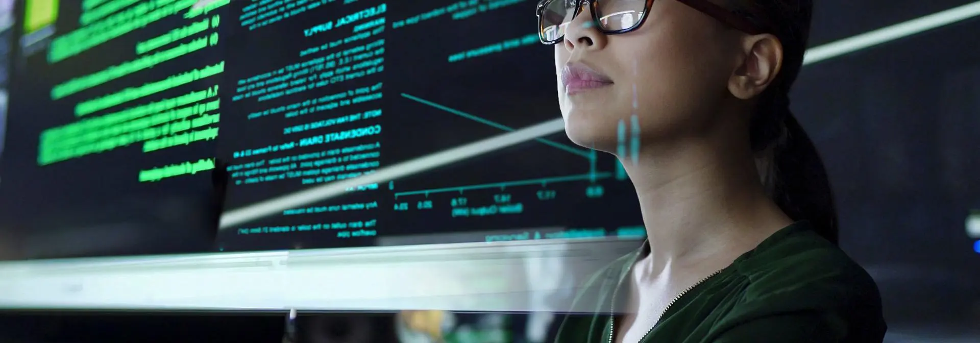 A woman wearing glasses studies computer code on a large screen
