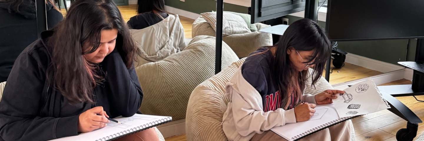 Two students sitting and drawing on sketch pads.