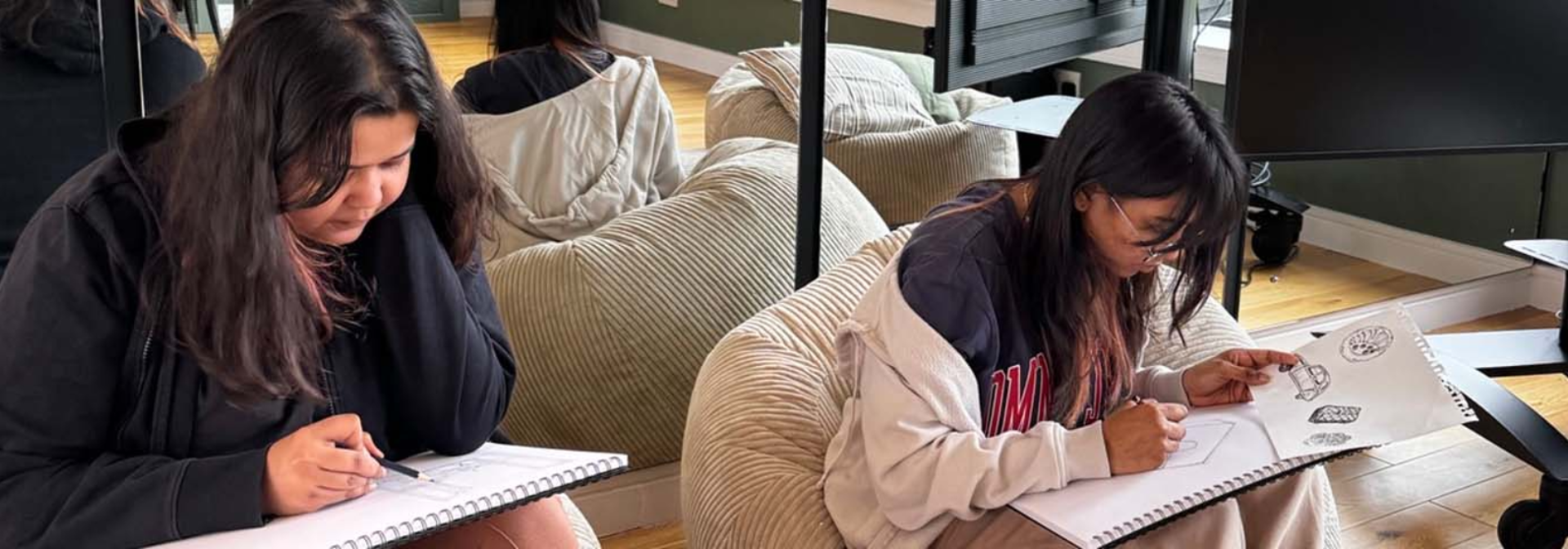 Two students sitting and drawing on sketch pads.