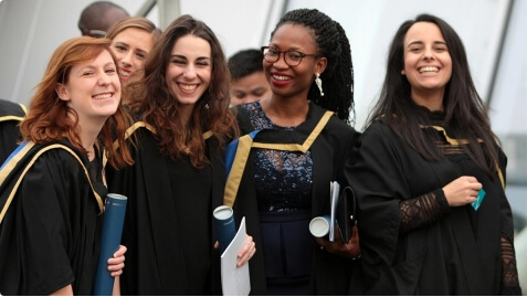 Graduates in gowns holding degrees and smiling