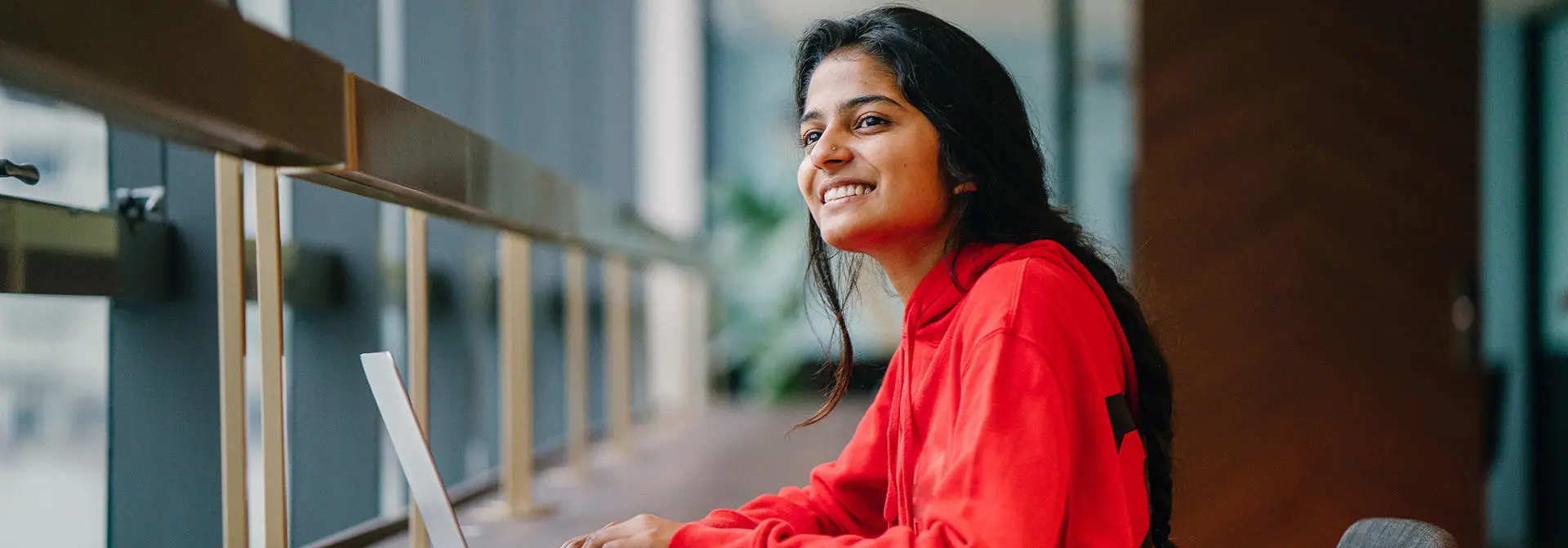 A student looks out of the window while working at her laptop.