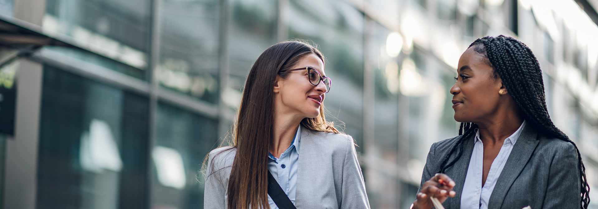 Two individuals in business attire walking and talking beside a modern building.