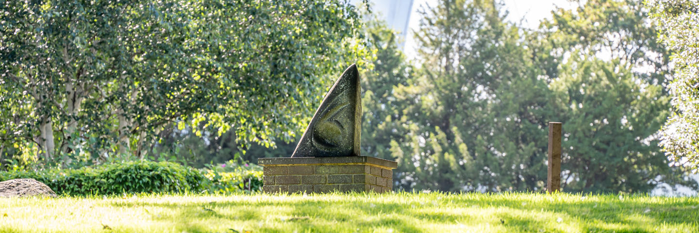 Triangular statue on a patch of grass.