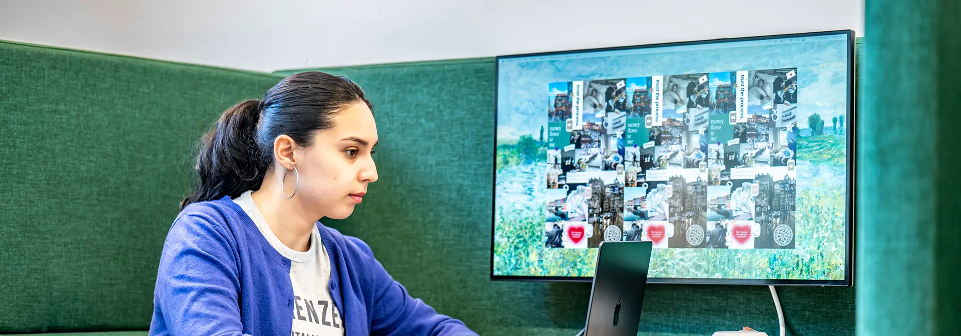 A female looking at a laptop in a comfortable looking booth with a second monitor connected