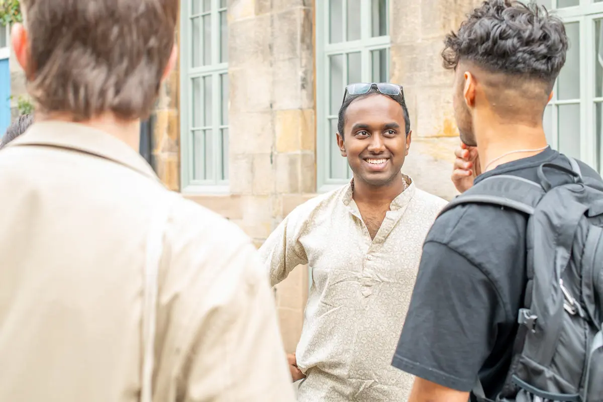 A smiling man speak with two individuals beside a stone wall.