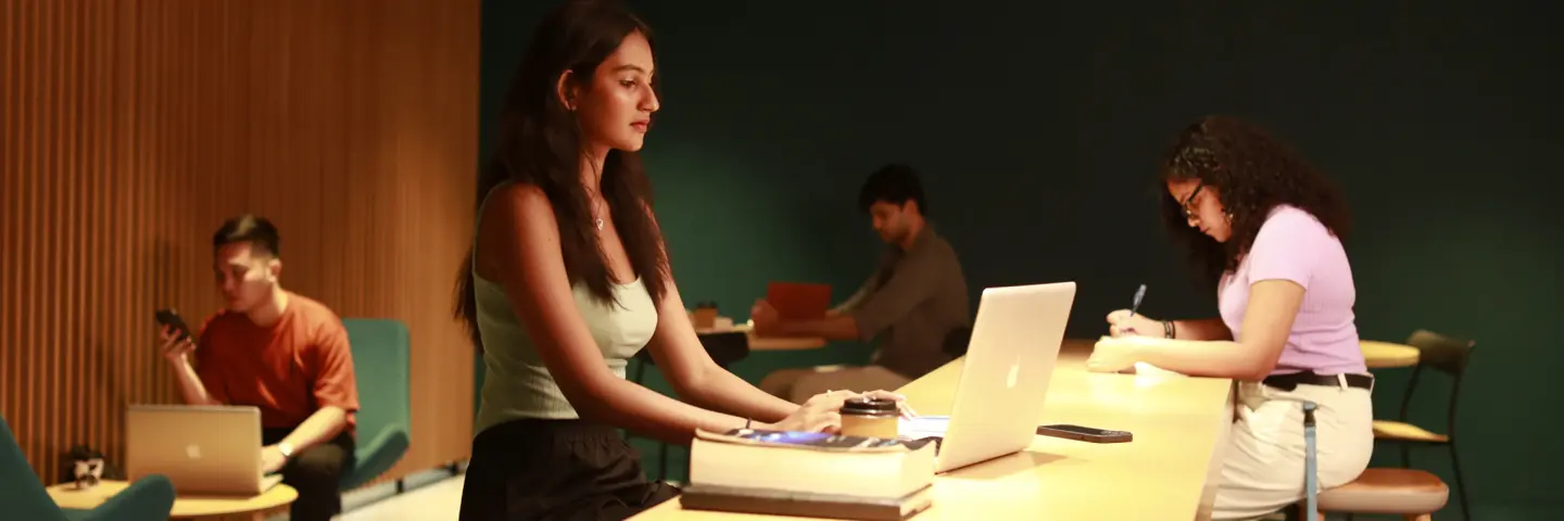Students sitting in a cafe studying with laptops and writing notes.