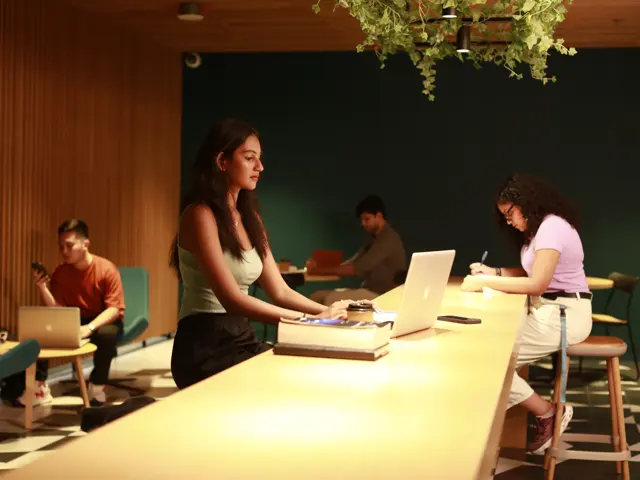 Students sitting in a cafe studying with laptops and writing notes.