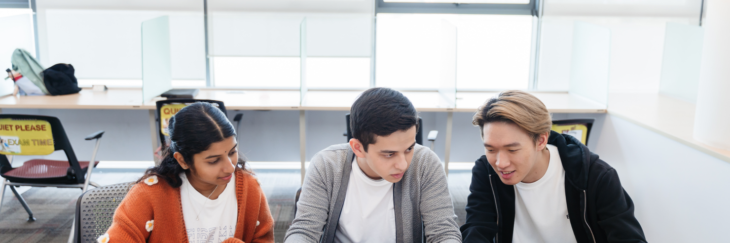 Two individuals sitting at a desk speaking to a staff member at Heriot-Watt