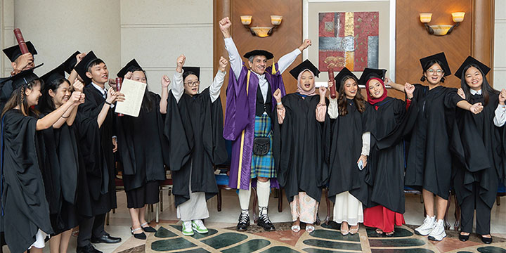 A group of Malaysia graduates and Professor Mushtak Al-Atabi raise their arms in celebration