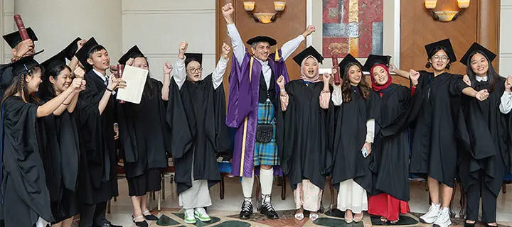 A group of Malaysia graduates and Professor Mushtak Al-Atabi raise their arms in celebration