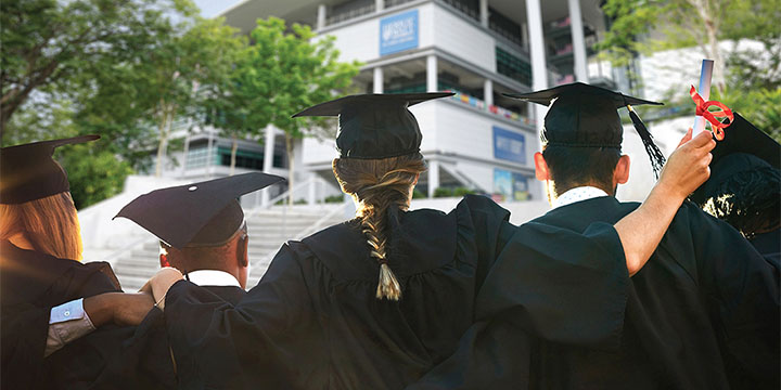 A group of graduates link arms while facing the Malaysia Campus building