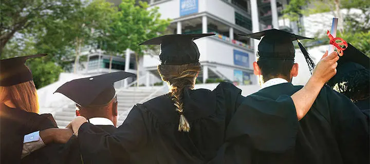 A group of graduates link arms while facing the Malaysia Campus building