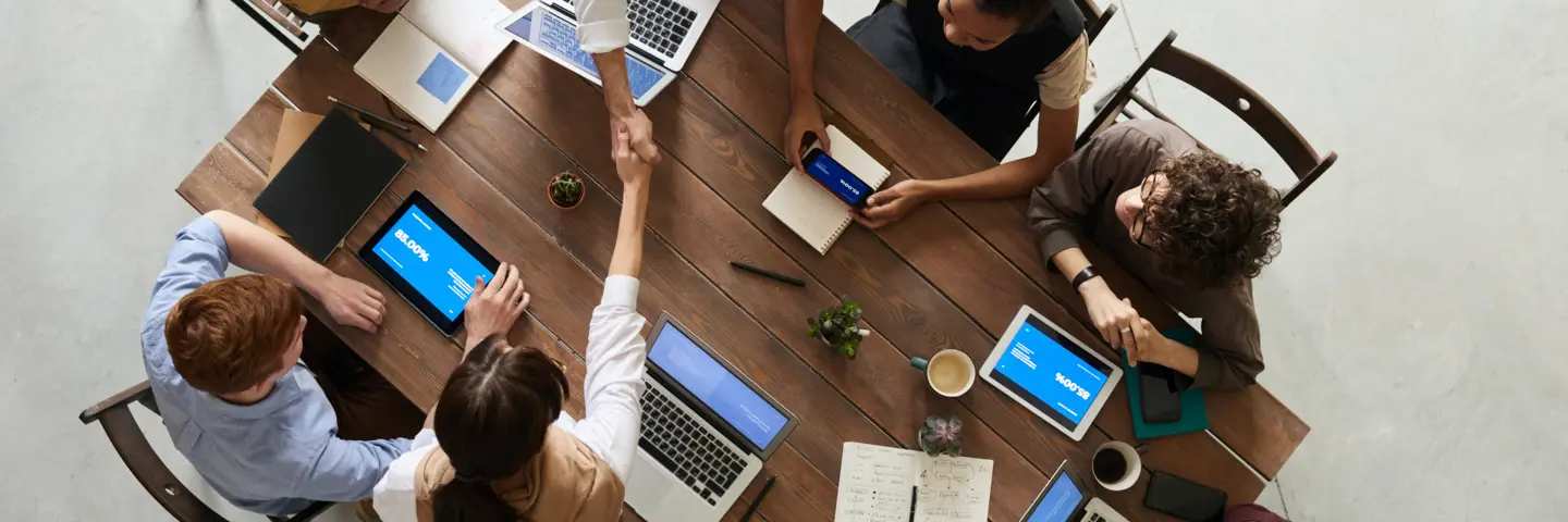 A birds-eye view of two people shaking hands over a table at a meeting.