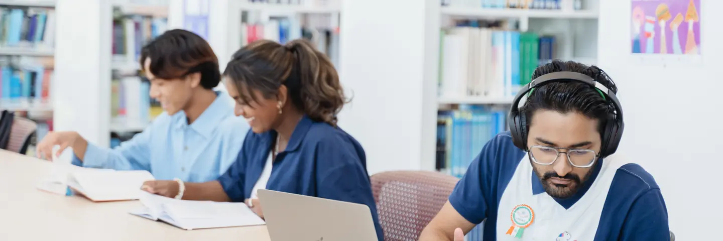 Three individuals work in a library with books and a laptop.