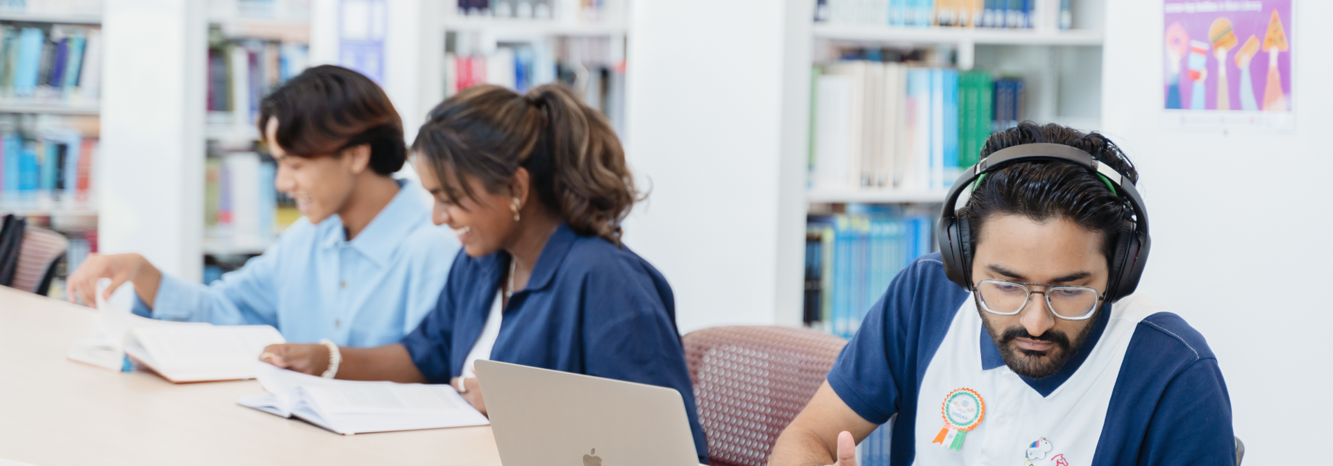 Three individuals work in a library with books and a laptop.