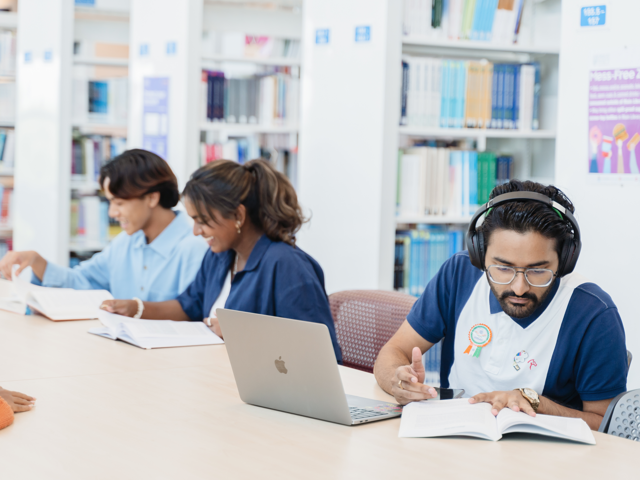 Three individuals work in a library with books and a laptop.